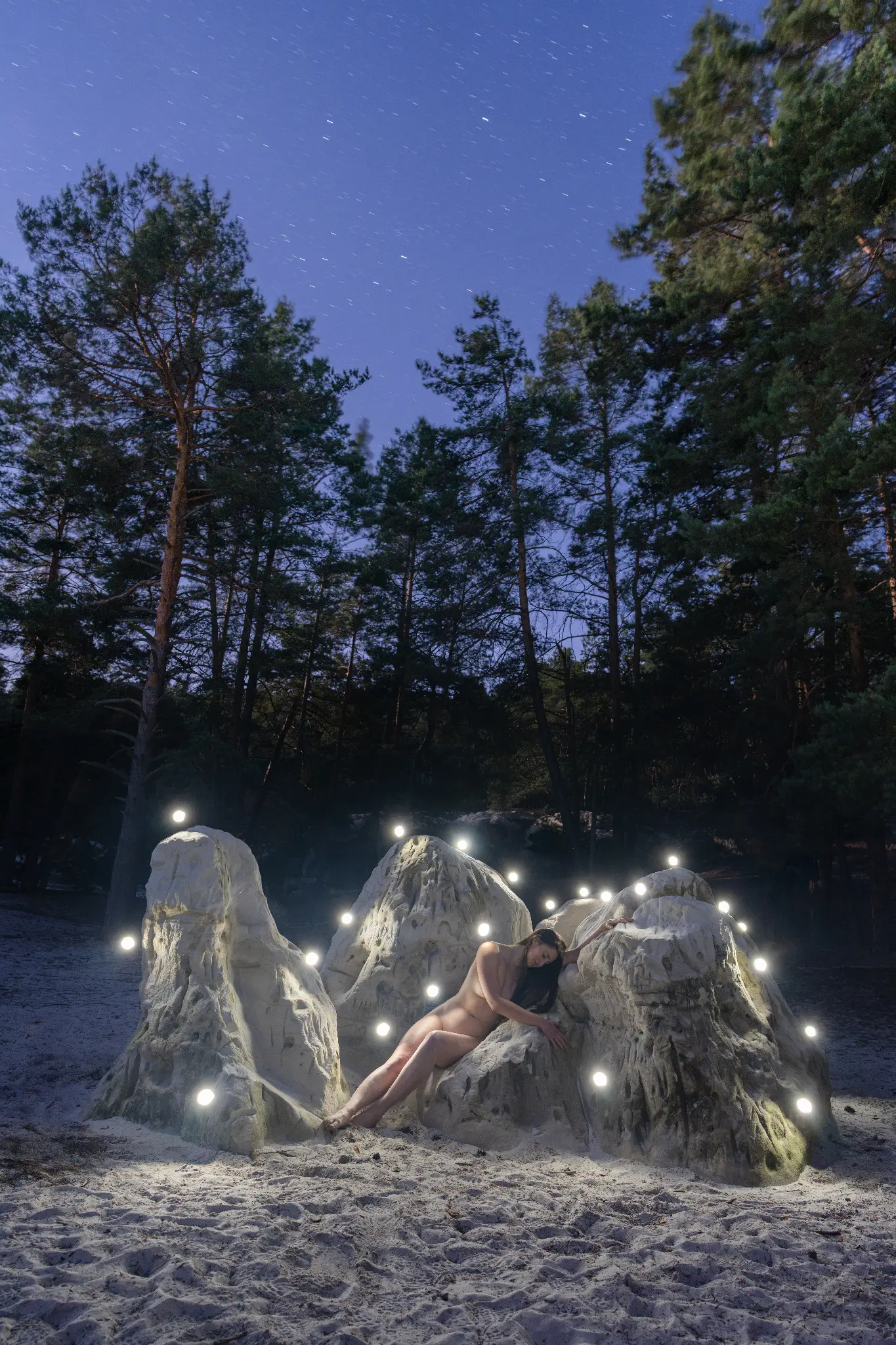 Nackte Figur zwischen mit Lichtpunkten markierten Sandsteinfelsen unter Sternenhimmel