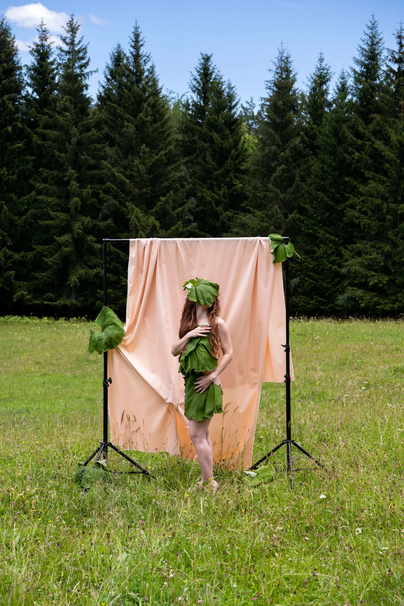 Mit Blättern bedeckte Figur vor rosafarbenem Hintergrund in einer Waldlichtung